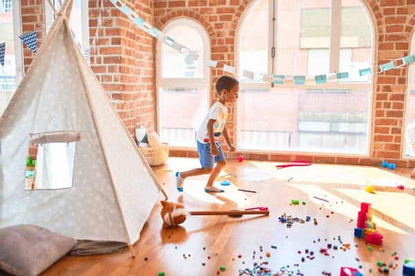 Güzel Afrikalı Amerikalı çocuk kreşteki oyuncakların etrafında durup gülümsüyor.
