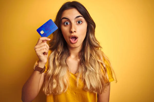 Młoda Piękna Kobieta Trzymająca Kartę Kredytową Żółtym Odizolowanym Tle Przerażona — Zdjęcie stockowe