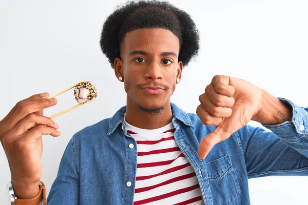 年轻的非洲裔美国男子吃寿司用筷子在孤立的白色背景与愤怒的脸 负面的迹象显示不喜欢与拇指向下 拒绝概念 — 图库照片