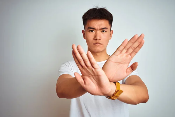 孤立した白い背景の上に立ってTシャツを着て若いアジア系中国人男性否定的な記号を行う腕と手のひらを横断拒否式 怒りの顔 — ストック写真