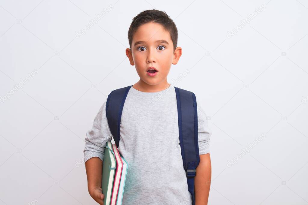 Beautiful student kid boy wearing backpack holding books over isolated white background scared in shock with a surprise face, afraid and excited with fear expression
