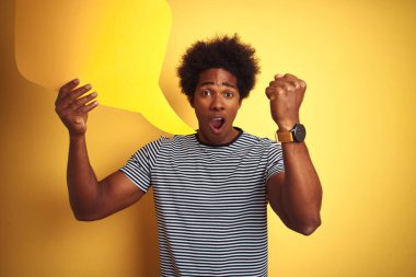 Young african american man holding speech bubble standing over isolated yellow background annoyed and frustrated shouting with anger, crazy and yelling with raised hand, anger concept