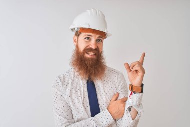 İzole edilmiş beyaz arka plan üzerinde güvenlik kaskı takan genç kızıl saçlı mimar yüzünde kocaman bir gülümsemeyle kameraya el ve parmak ile bakıyor..