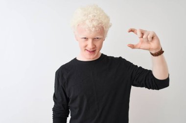 Siyah tişörtlü genç albino adam izole edilmiş beyaz arka plan üzerinde duruyor gülümsüyor ve el hareketleriyle küçük boy işareti yapıyor ve kameraya bakıyor. Ölçü kavramı.