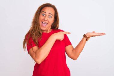 Orta yaşlı olgun bir kadın, beyaz izole edilmiş arka planda durup hayrete düşmüş ve kameraya gülümserken eliyle ve parmağıyla işaret ediyor..