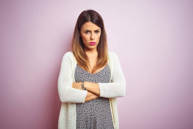 Pembe izole edilmiş arka planda duran genç ve güzel bir kadın şüpheci ve gergin, yüzünde çapraz kollu tasvip etmeyen bir ifade. Negatif kişi.
