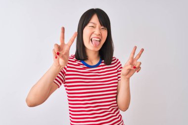 İzole edilmiş beyaz arka plan üzerinde kırmızı çizgili tişört giyen genç ve güzel Çinli kadın iki elini de zafer işareti yaparken gösteren bir dille gülümsüyor. İki numara..