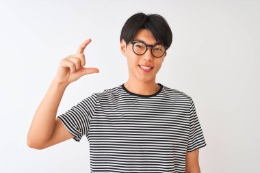 Gözlüklü ve donanma tişörtlü Çinli bir adam izole edilmiş beyaz arka planda duruyor gülümsüyor ve el hareketleriyle küçük boy işareti yapıyor ve kameraya bakıyor. Ölçü kavramı.