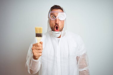 Profesyonel işçi teçhizatı giyen ressam arka planda fırça tutuyor. Şaşırmış bir yüz ifadesinden korkuyor ve heyecanlanıyor.