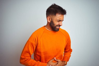 İzole edilmiş beyaz arka plan üzerine turuncu kazak giyen genç Hintli adam midesi üzerinde el ele çünkü hazımsızlık, acı verici bir hastalık kendini iyi hissetmiyor. Ache kavramı.