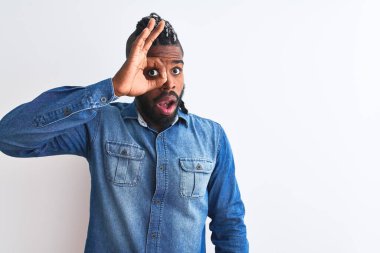 Beyaz arka planda kot gömlek giyen, saçları örgülü Afro-Amerikan bir adam şaşırmış yüz ifadesiyle şaşırmış, parmaklarından bakan bir jest yapıyor. İnançsız ifade.