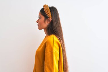 Sarı süveter ve diadem giyen genç güzel bir kadın yalıtılmış beyaz arka plana bakıyor, rahat profil pozu veriyor kendine güveni tam bir gülümsemeyle..