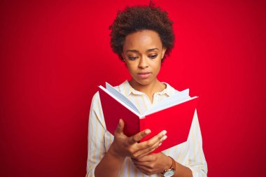 Afro-Amerikalı bir kadın, kırmızı izole edilmiş arka plan üzerine kitap okuyor. Zeki bir yüz ifadesiyle ciddi olduğunu düşünüyor.