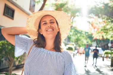 Genç ve güzel bir kadın mutlu bir şekilde gülümsüyor güneşli bir yaz gününde şehir sokaklarında yürüyor.