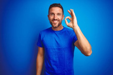 Mavi izole edilmiş arka planda rahat tişört giyen yakışıklı genç adam el ve parmaklarıyla 