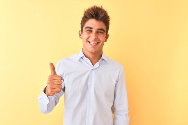 Sarı arka planda zarif gömlekler giyen genç yakışıklı iş adamı mutlu bir el hareketi yapıyor. Kameraya bakıp başarıyı gösteren ifade onaylanıyor.