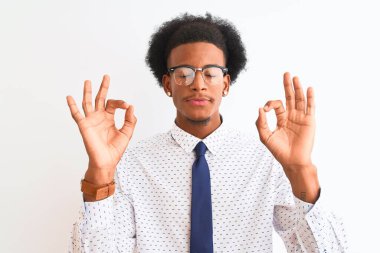 Genç Afrikalı Amerikalı iş adamı, izole edilmiş beyaz arka planda kravat ve gözlük takıyor rahatlıyor ve parmaklarıyla meditasyon hareketi yaparken gözleri kapalı gülümsüyor. Yoga konsepti.