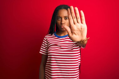 Çizgili tişört giyen genç Afro-Amerikalı kadın izole edilmiş kırmızı arka planda dikiliyor ve avuç içiyle şarkı söylemeyi kesiyor. Yüzünde olumsuz ve ciddi bir jest olan uyarı ifadesi.