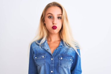 İzole edilmiş beyaz arka plan üzerinde dikilmiş sıradan kot gömlek giyen güzel bir kadın komik yüzüyle yanaklarını şişiriyor. Havayla şişmiş ağız, çılgın bir ifade..