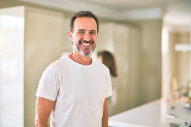 Orta yaşlı yakışıklı adam mutfakta gülümsüyor.