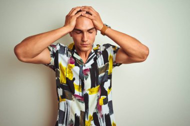 Beyaz tenli arka planda yaz tişörtü giyen yakışıklı genç adam acı ve migren yüzünden çaresiz ve stresli bir baş ağrısı çekiyor. Ellerini başının üstüne koy..