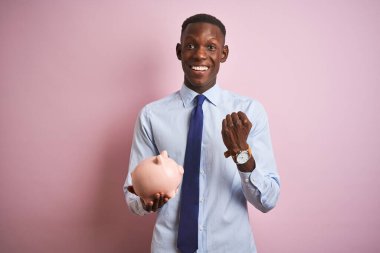 Afrikalı Amerikalı işadamı domuzcuk kumbarasını soyutlanmış pembe arka planda duruyor gururla bağırıyor, zaferi ve başarıyı kutluyor çok heyecanlı, coşkulu bir duygu.