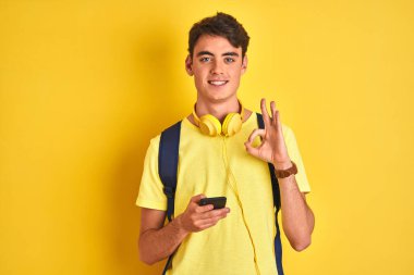Kulaklık takan ve izole edilmiş arka planda akıllı telefon kullanan genç bir çocuk parmaklarıyla imza atıyor, mükemmel bir sembol.