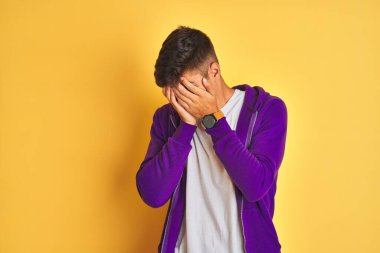 Mor kazak giyen genç Hintli adam izole edilmiş sarı arka planda dikiliyor. Ağlarken suratını ellerle kapatıyor. Depresyon kavramı.