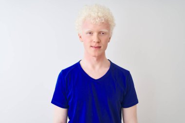 Mavi günlük tişört giyen genç, albino sarışın adam izole edilmiş beyaz arka planda duruyor ve yüzünde ciddi bir ifade var. Basit ve doğal bir şekilde kameraya bakıyorsun..