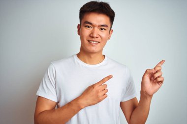 Asyalı genç bir Çinli tişört giyiyor. İzole edilmiş beyaz arka planda duruyor. Gülümsüyor ve kameraya bakıyor..