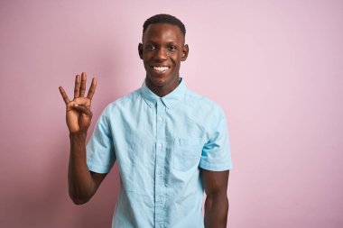Mavi gömlekli Afro-Amerikalı bir adam pembe arka planda dikiliyor ve parmaklarını dört numaraya doğrultuyor. Kendinden emin ve mutlu gülümsüyor..