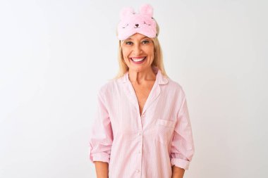 Yüzünde mutlu ve havalı bir gülümsemeyle izole edilmiş beyaz arka plan üzerinde uyku maskesi ve pijama giyen orta yaşlı bir kadın. Şanslı kişi..