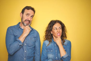 Güzel bir orta yaşlı çift, yalıtılmış sarı arka planda durup bir soru hakkında endişeleniyorlar, endişeli ve sinirliler.