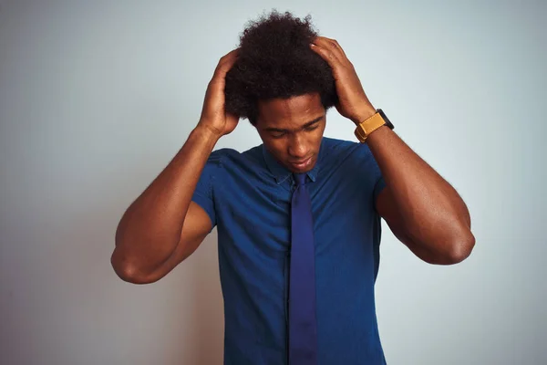 American business man with afro hair wearing blue shirt and tie over isolated white background suffering from headache desperate and stressed because pain and migraine. Hands on head.