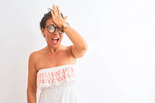 Middle age woman wearing casual dress and glasses standing over isolated white background surprised with hand on head for mistake, remember error. Forgot, bad memory concept.