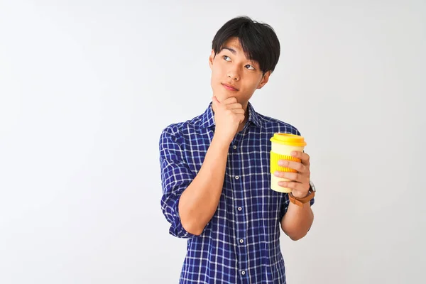 Young chinese man drinking take away coffee standing over isolated white background serious face thinking about question, very confused idea