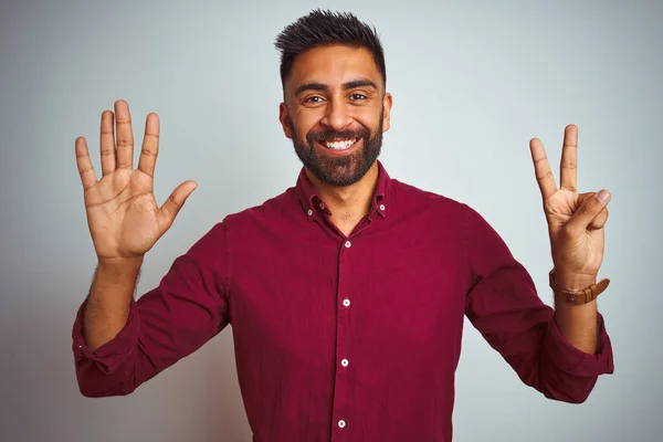 若いですインド人男性身に着けています赤いエレガントなシャツを身に着けています上の隔離されたグレーの背景を示すと指の番号7と指摘しながら笑顔自信と幸せ — ストック写真