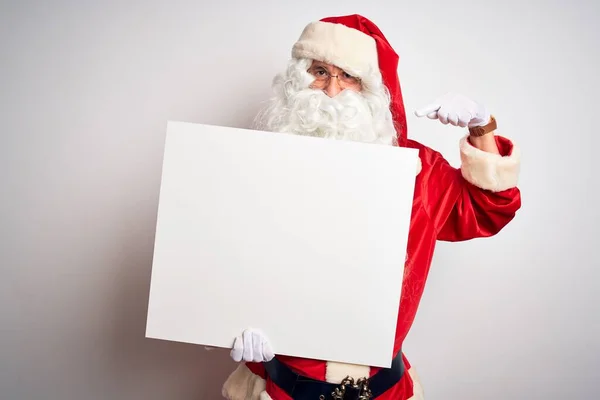 中年男子身穿圣诞老人服装 拿着横幅挂在孤立的白色背景上 满脸惊讶地指着自己 — 图库照片