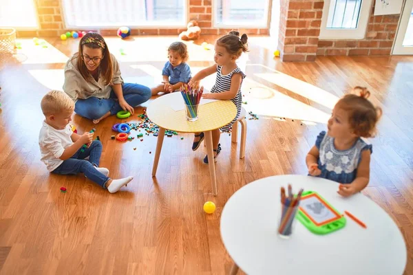 Beautiful teacher and group of toddlers playing around lots of toys at kindergarten