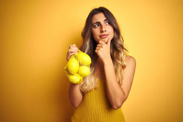Молодая Красивая Женщина Держит Сеть Лимонов Желтом Изолированном Фоне Серьезное — стоковое фото