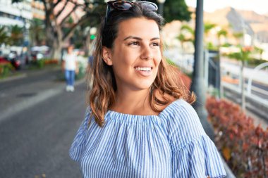 Genç ve güzel bir kadın mutlu bir şekilde gülümsüyor güneşli bir yaz gününde şehir sokaklarında yürüyor.