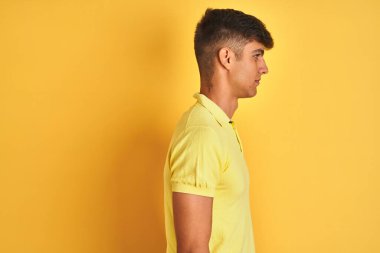 Sıradan polo giyen genç Hintli adam, yalıtılmış sarı arka planda duruyor, yan yana bakıyor, rahat profil pozu veriyor, kendine güvenen bir gülümsemesi var..