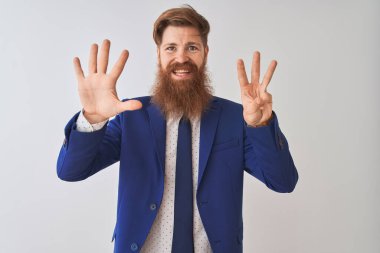 İzole edilmiş beyaz arka plan üzerinde duran genç kızıl saçlı iş adamı sekiz numaralı parmaklarıyla gülümseyerek kendinden emin ve mutlu görünüyor..