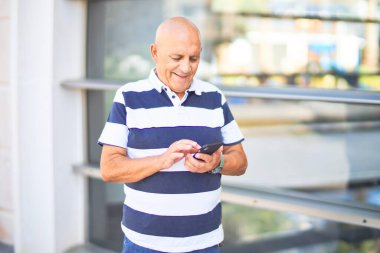 Kıdemli yakışıklı adam mutlu ve kendinden emin gülümsüyor. Yüzünde gülümsemeyle şehrin caddesinde akıllı telefon kullanarak dikiliyorsun.