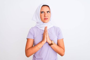 İzole edilmiş beyaz arka plan üzerinde tesettürlü genç, güzel bir Arap kız. Yüzünde umut ifadesi olan ve endişeli bir şekilde el ele yalvarıp dua ediyor. Af diliyor. Din kavramı.