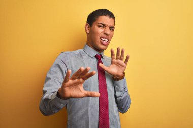 Yakışıklı Arap iş adamı gömleği ve kravat takıp izole edilmiş sarı arka plan üzerinde korku ifadesi karşısında korkmuş ve dehşete düşmüş. El hareketlerini durdur, şok içinde bağır. Panik konsepti.