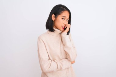 Balıkçı yaka kazak giyen genç bir kadın izole edilmiş beyaz arka planda duruyor. Elleri ağızdan tırnak yerken gergin ve stresli görünüyor. Endişe sorunu.