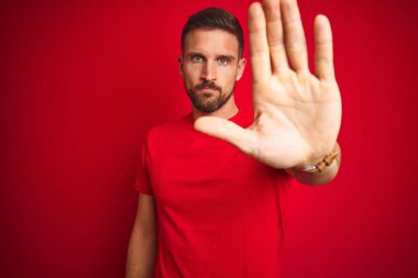 Kırmızı izole edilmiş arka plan üzerine gündelik tişört giyen yakışıklı genç adam avucunun içi gibi şarkı söylemeyi kesiyor. Yüzünde olumsuz ve ciddi bir jest olan uyarı ifadesi.