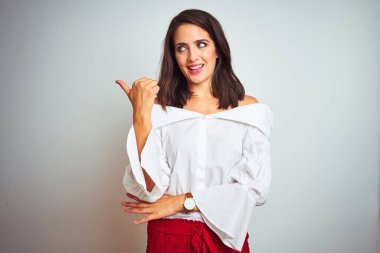 Beyaz izole arka plan üzerinde duran t-shirt giyen genç güzel kadın mutlu yüz görünümlü gülümseyerek ve başparmak ile yan işaret.