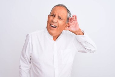 Üst düzey gri saçlı adam izole beyaz arka plan üzerinde ayakta zarif gömlek giyen el kulak üzerinde bir söylenti veya dedikodu bir işitme dinlerken gülümseyerek. Sağırlık kavramı.